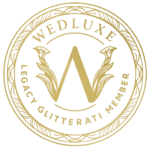 Gold circular emblem with ornate border, featuring a large "W" in the center surrounded by stylized leaves. Text along the edge reads "WEDLUXE LEGACY GLITTERATI MEMBER," ideal for top Wedding Menswear Suit Toronto professionals.