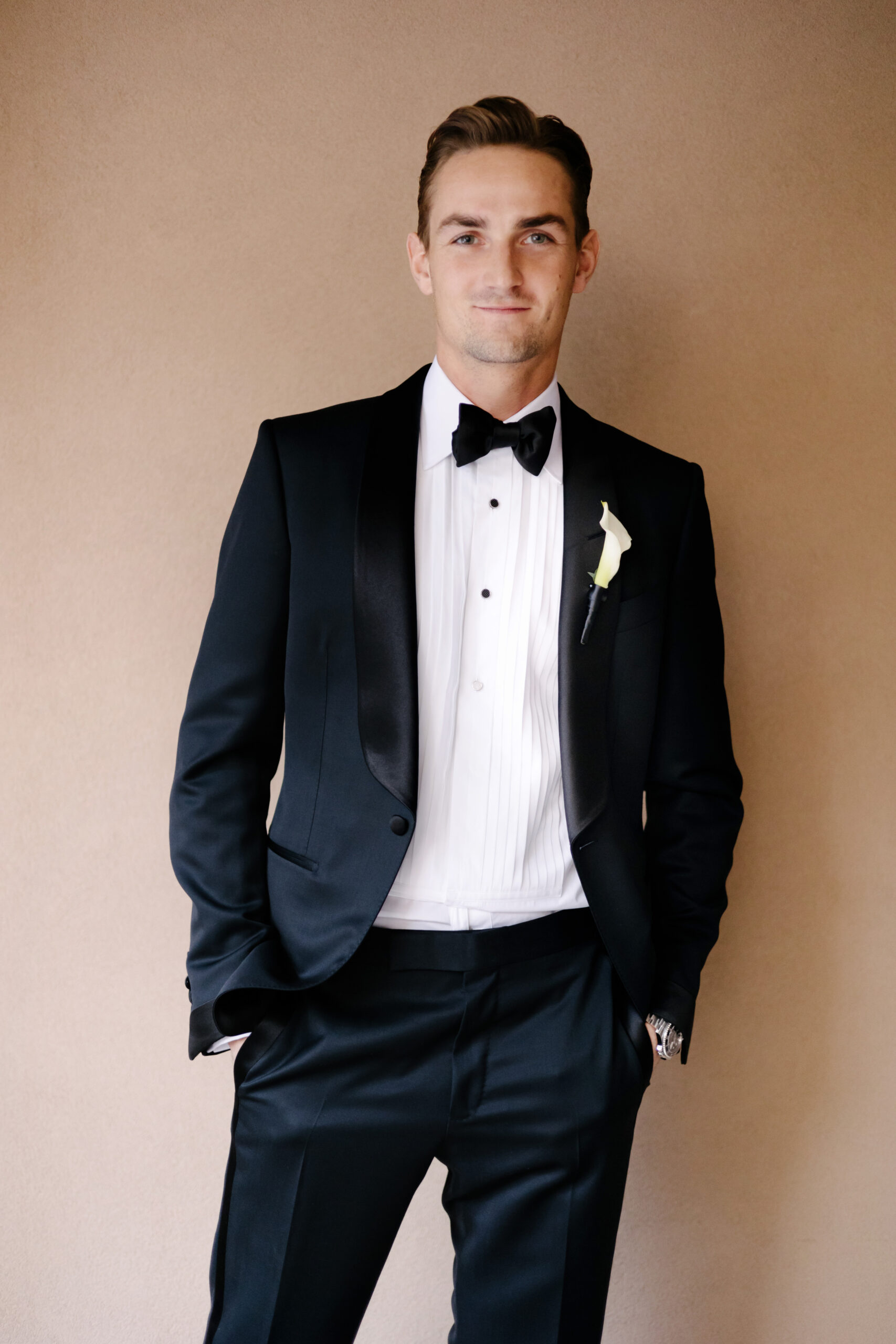 A man in a black tuxedo with a white shirt and black bow tie stands ...
