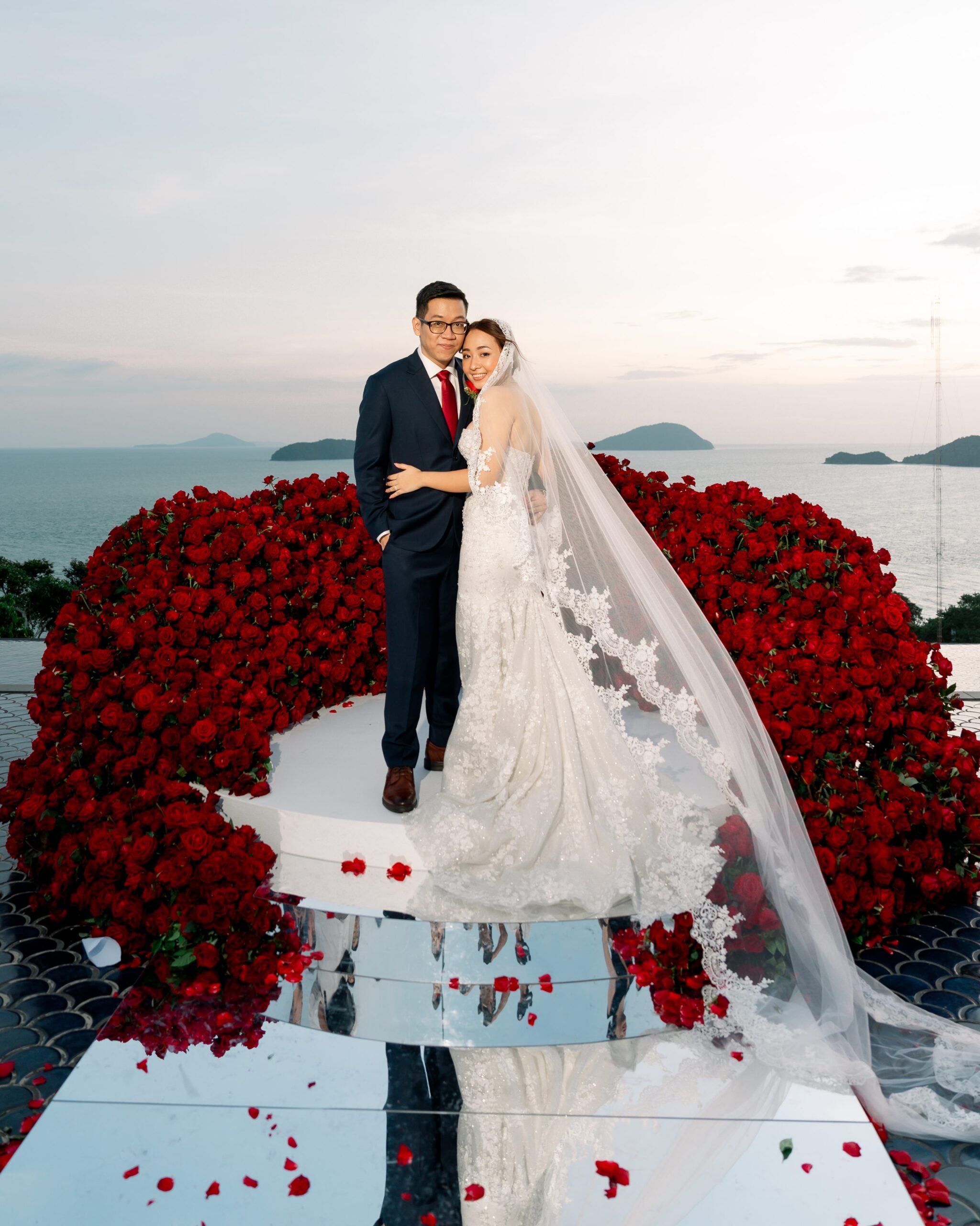 A bride in a lace gown and veil stands with her groom on a white platform, A bride in a lace gown and veil stands with her groom on a white platform,
