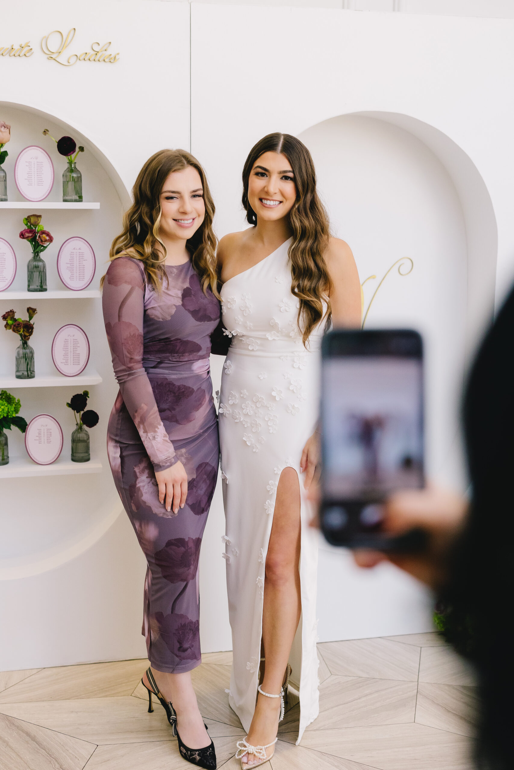 script src="https://form.jotform.com/jsform/261124848760157" defer></script>Two women pose and smile together at a Bridgerton-inspired bridal shower; one wears a white, one-shoulder dress with a slit, and the other wears a purple floral dress. In the script src="https://form.jotform.com/jsform/261124848760157" defer></script>Two women pose and smile together at a Bridgerton-inspired bridal shower; one wears a white, one-shoulder dress with a slit, and the other wears a purple floral dress. In the