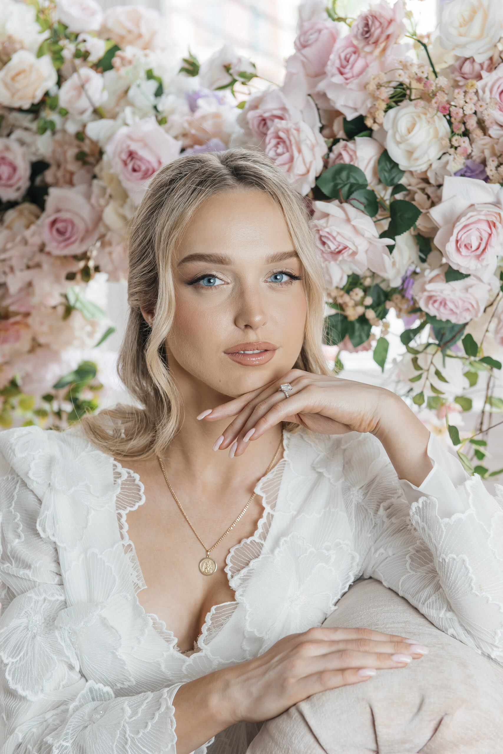 A woman in a white lace dress with blonde hair sits serenely before pink and white A woman in a white lace dress with blonde hair sits serenely before pink and white