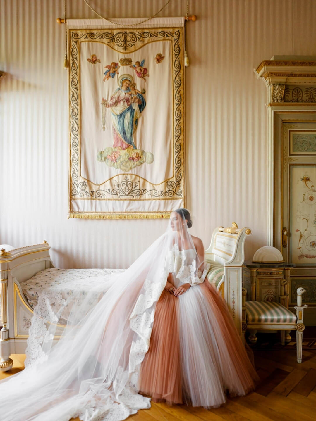 A bride in a voluminous ombr white and rust tulle gown with a long lace veil A bride in a voluminous ombr white and rust tulle gown with a long lace veil