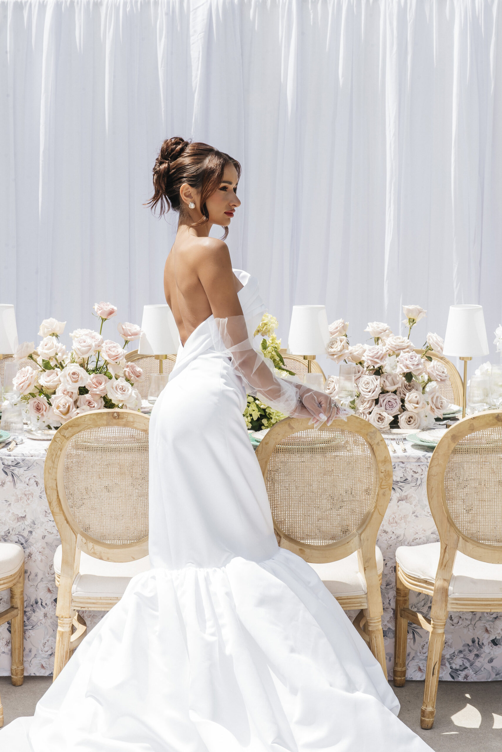script src="https://form.jotform.com/jsform/261124848760157"  defer></script>A bride in a strapless white gown and sheer gloves stands  beside an elegant table decorated with pastel flowers and candles, with  white drapery as a backdropcapturing Estate ...
