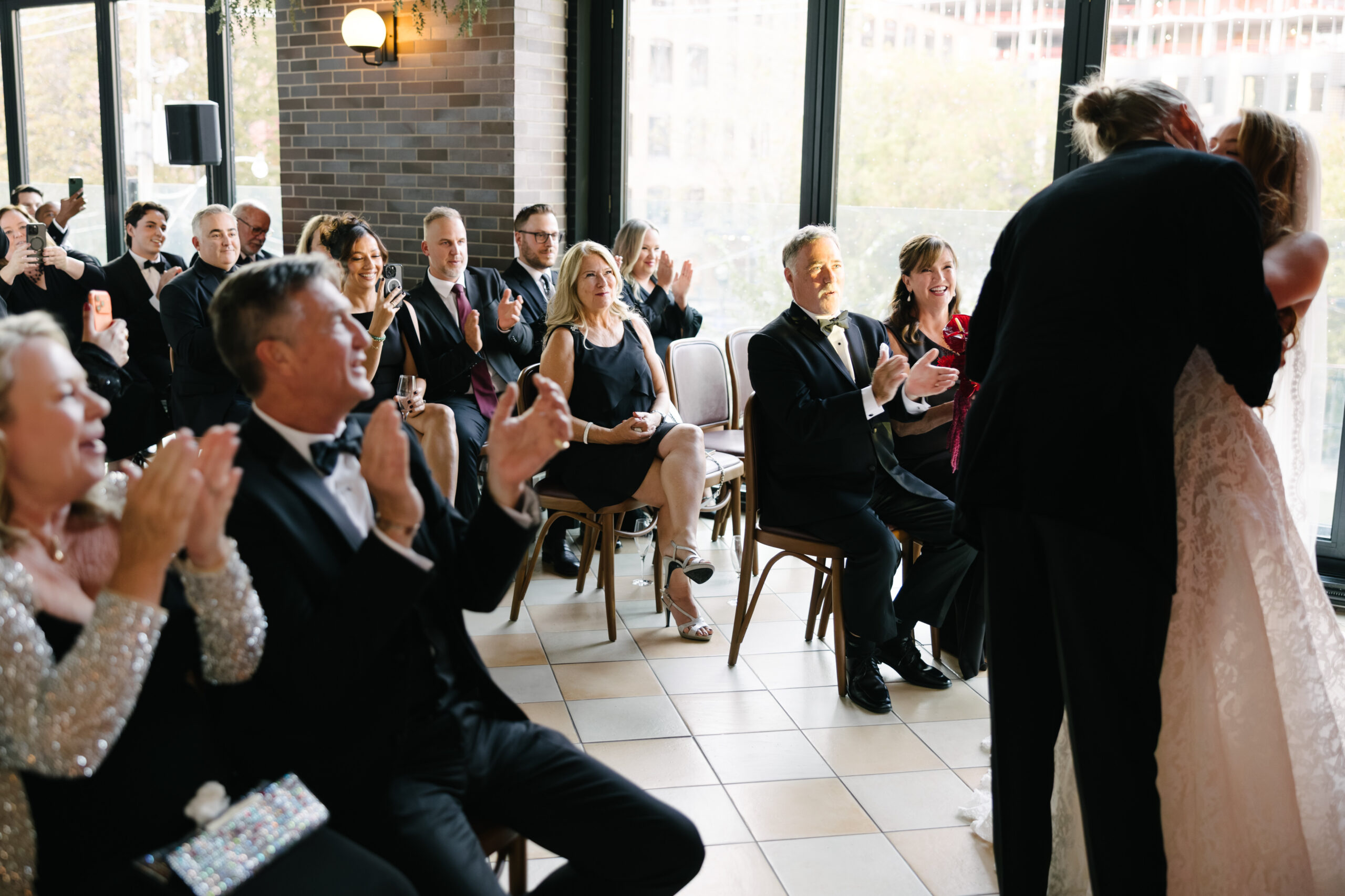 A bride and groom embrace at the front of a room as well-dressed guests ...