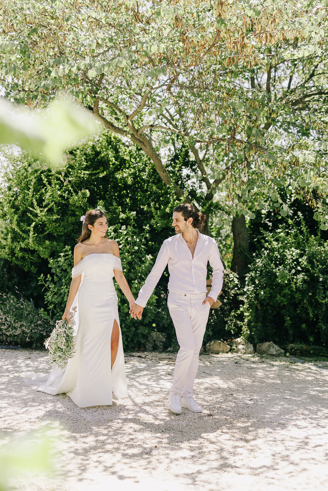 green italian wedding dress A bride in a white off-shoulder and a groom in light attire walk hand Summer festive edit