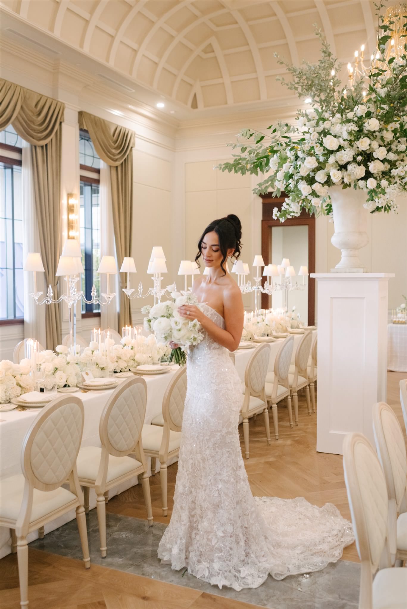 A bride in a lace wedding dress holds a bouquet and stands by an ...