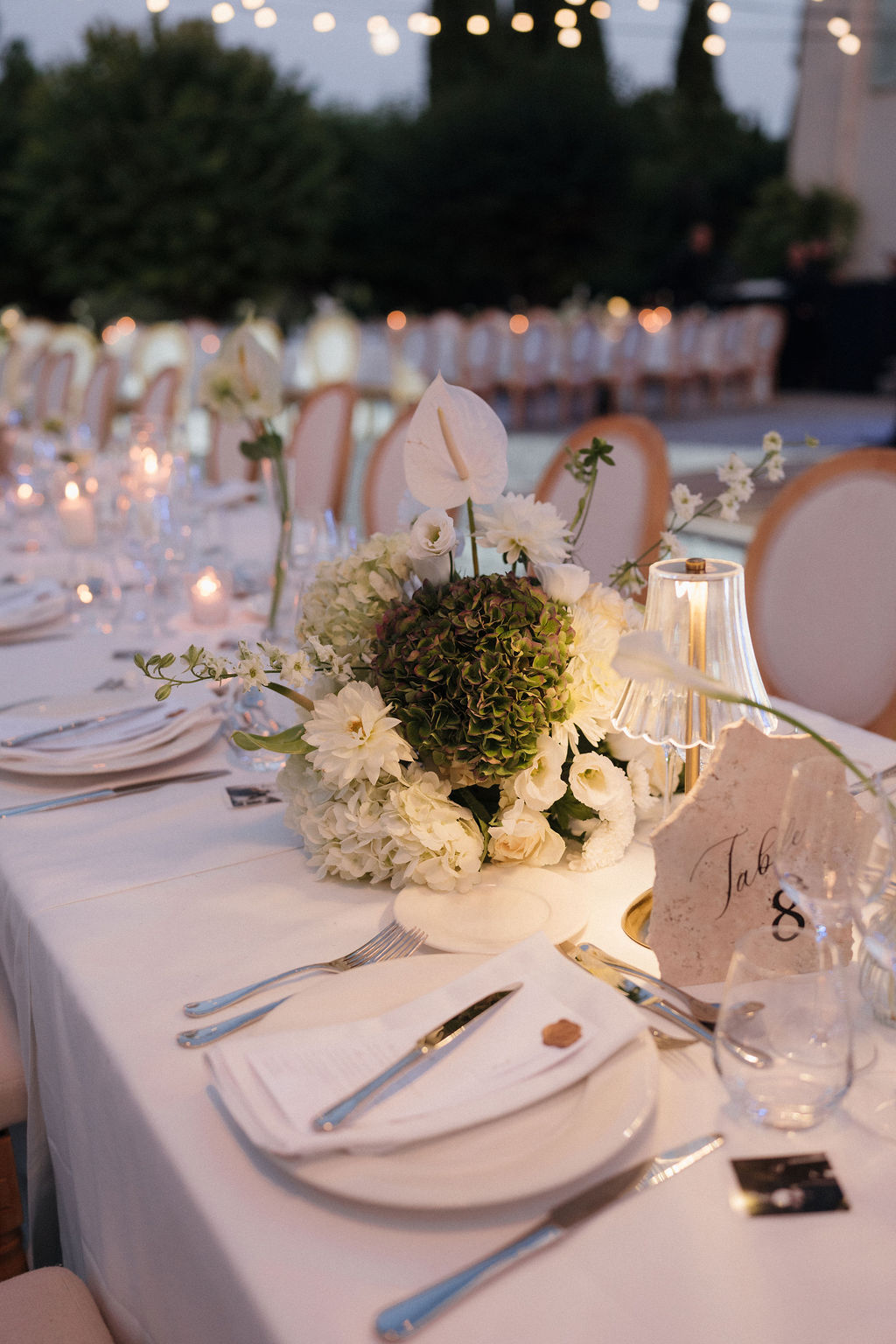 Elegant outdoor dinner table set with white linens, floral centerpiece ...