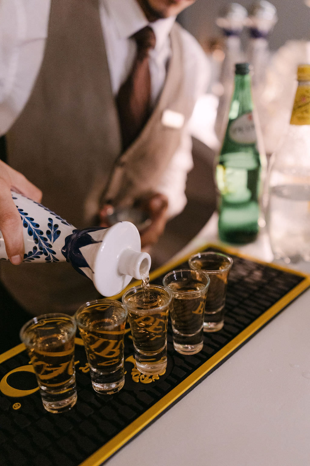 A bartender in a vest and tie pours clear liquor from a decorative ...