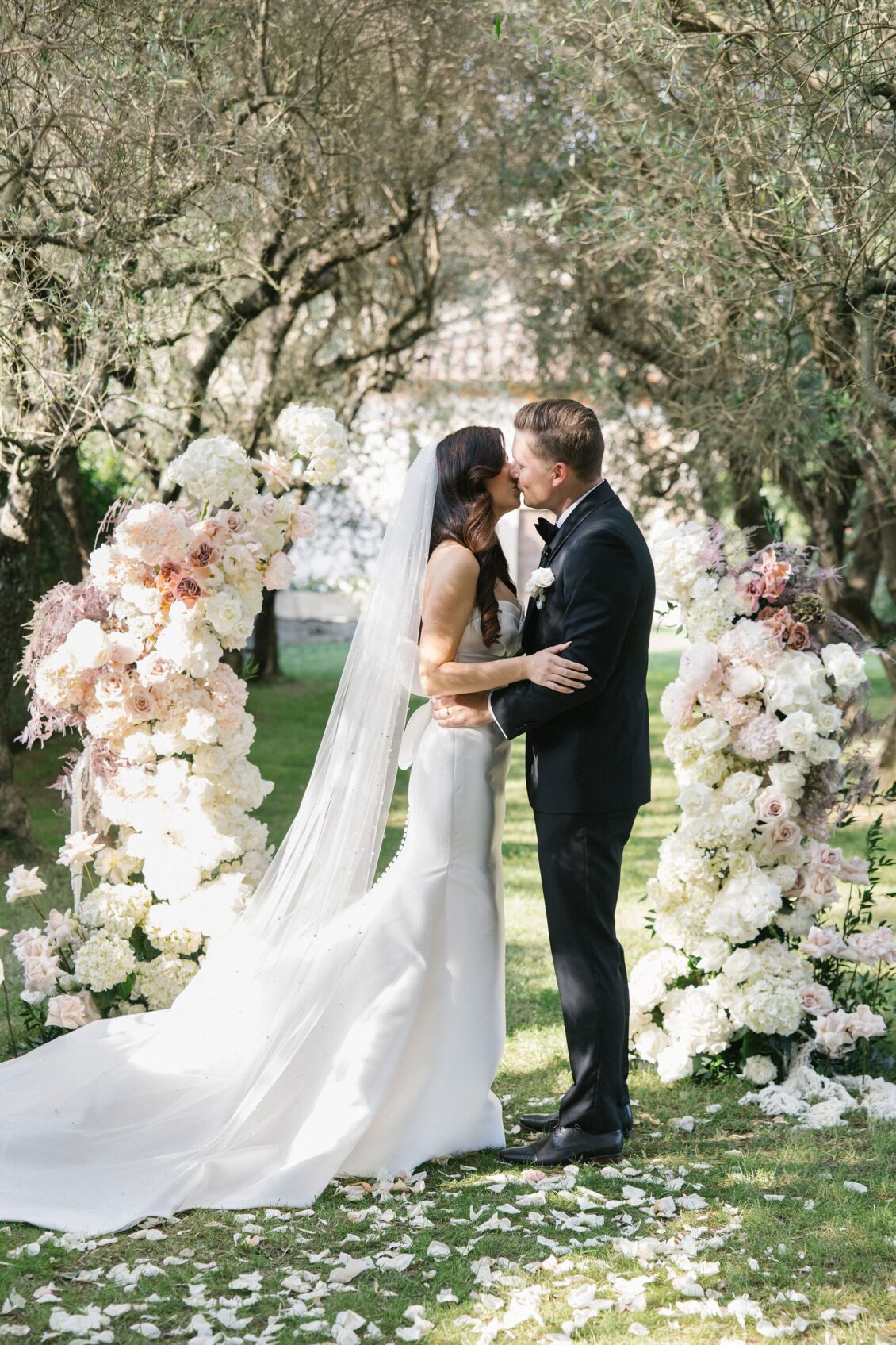 Jennifer and Travis kissing beneath the olive-tree floral arch