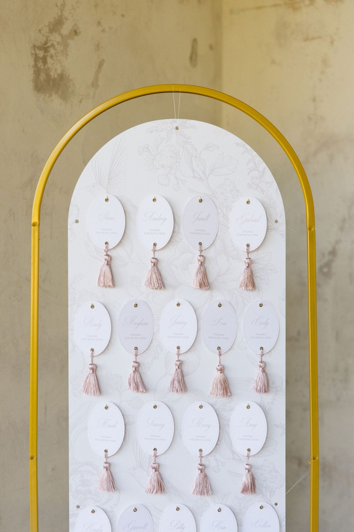 Arched blush escort-card display with tasselled name cards