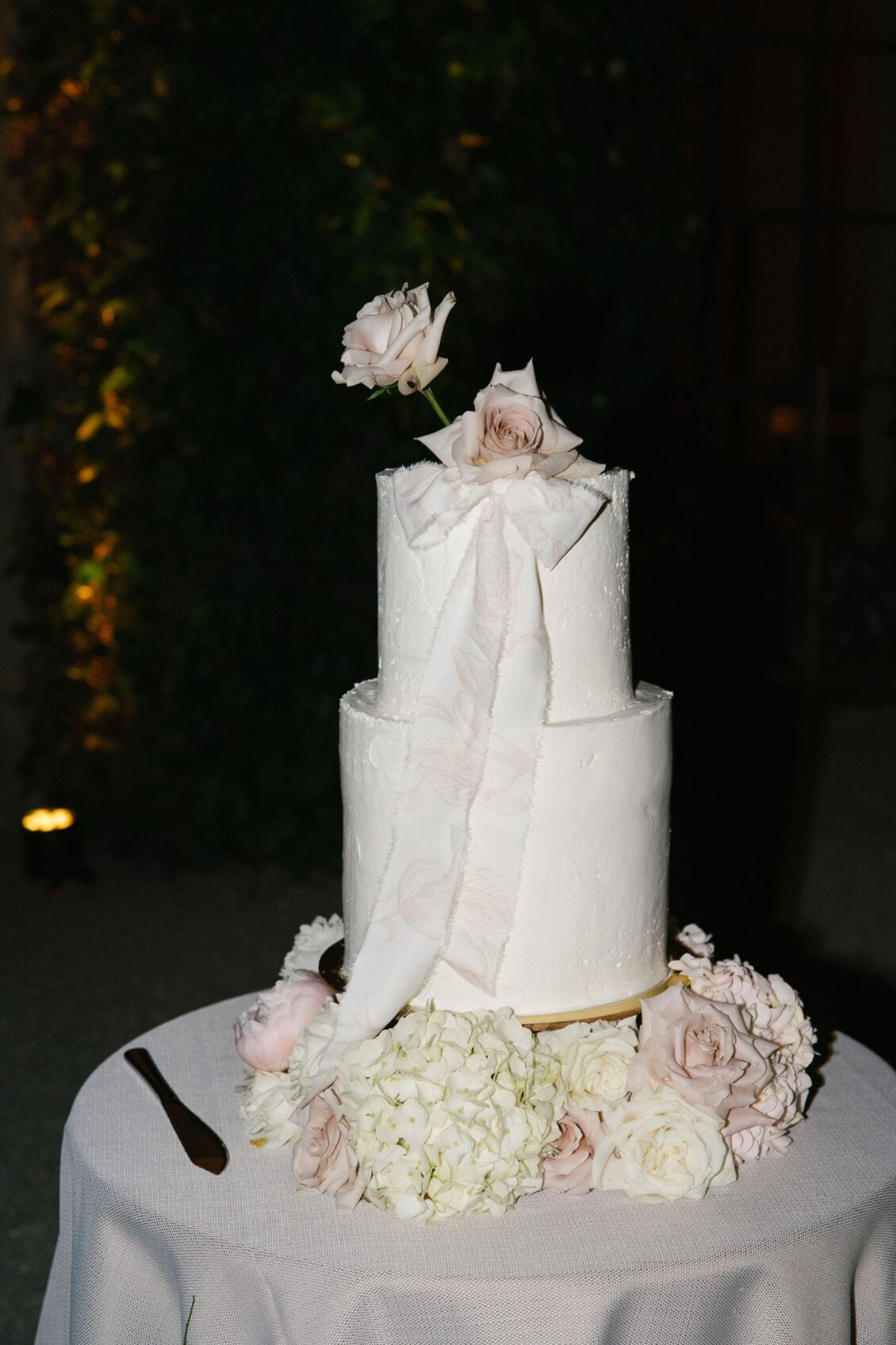 Modern white wedding cake with sculptural fondant bows and blush flowers