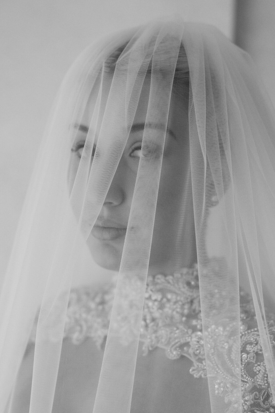 A black and white photo of a bride wearing a lace dress and a sheer veil covering her face, looking softly at the camera, captures the timeless elegance of the Ariana and Julian Borghese wedding.