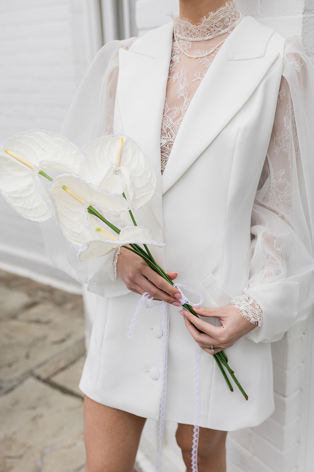 Cropped view of a model in a white blazer dress holding a bouquet of white anthuriums.