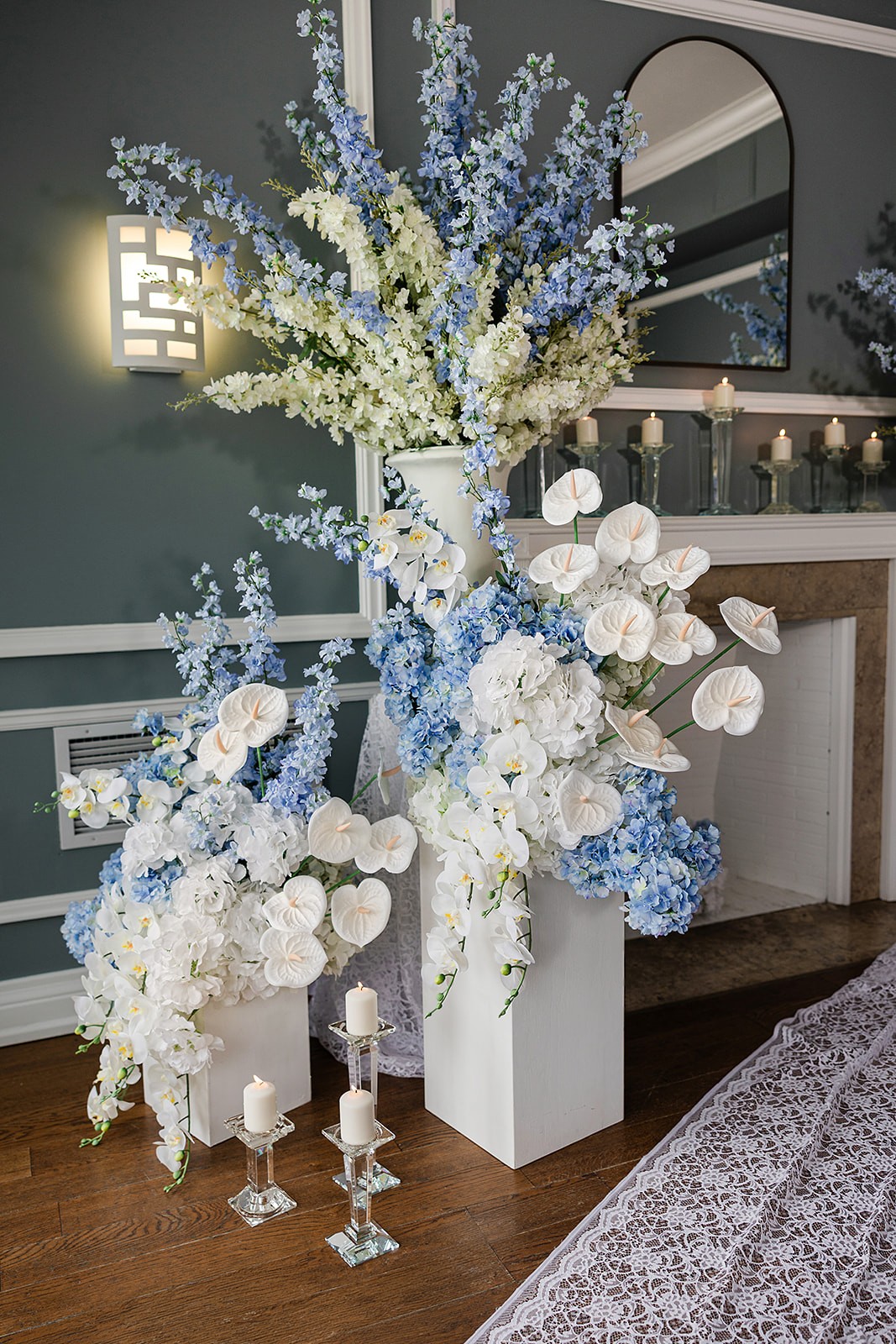 Tall blue-and-white floral installation in white pedestal vessels with glass taper candles.