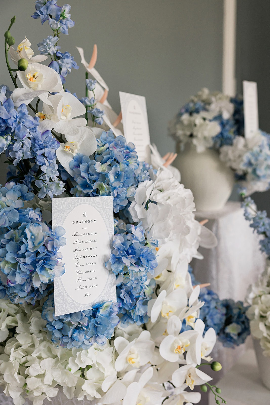 Narrow printed menu card nestled among blue hydrangeas, white orchids, and pale flowers.