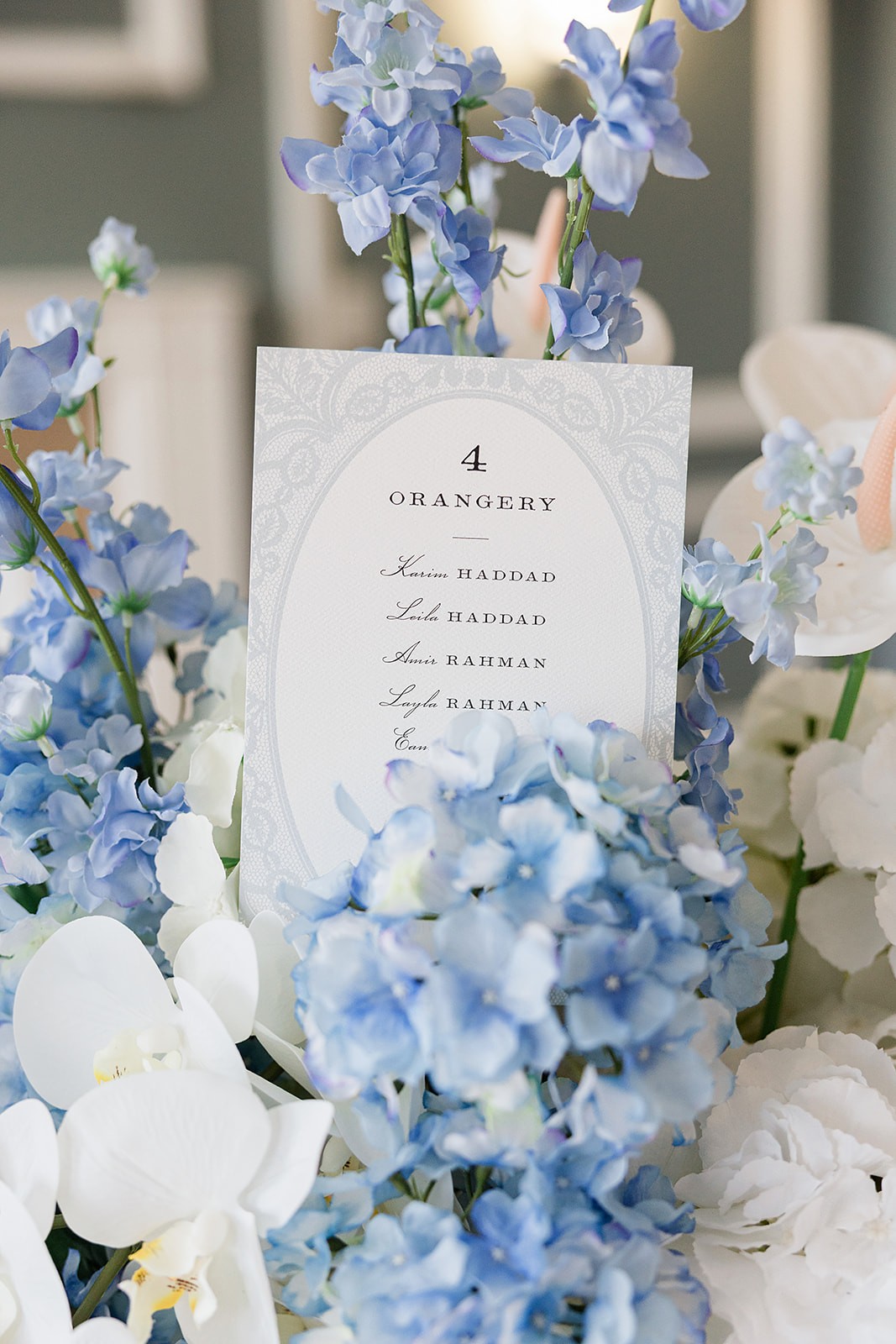 Printed menu card tucked into a dense arrangement of blue hydrangeas and white orchids.
