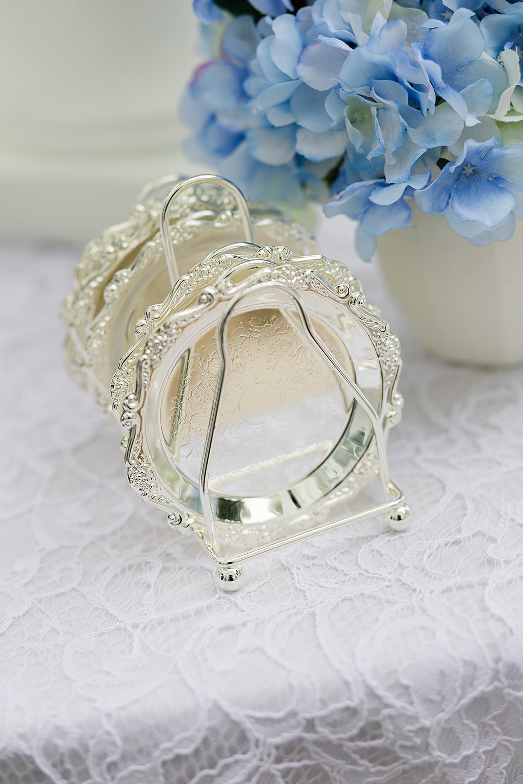 Small silver-toned jewellery piece displayed on white lace beside blue hydrangea petals.