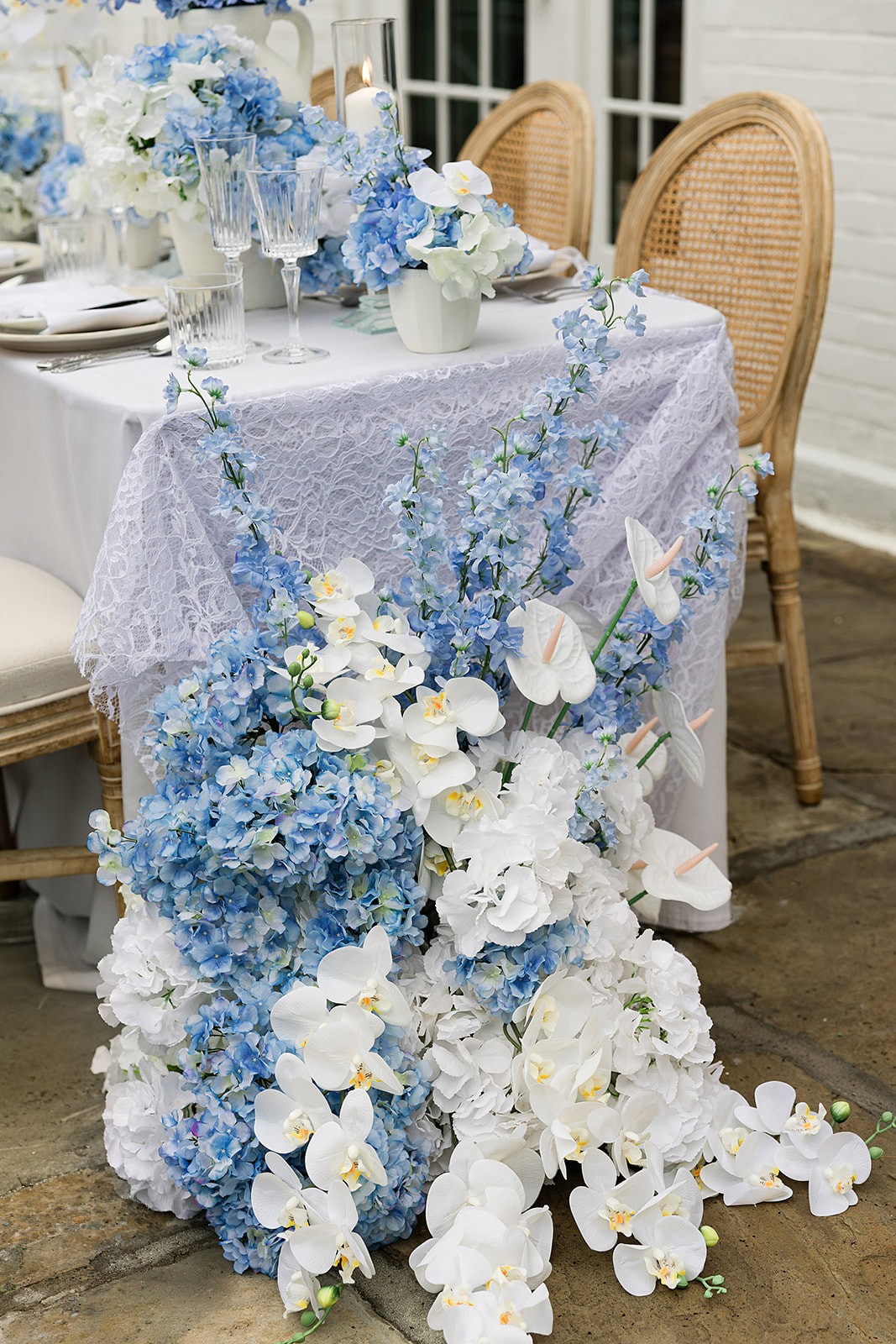 Blue-and-white flowers cascading from the end of a patterned reception table beside cane-back chairs.