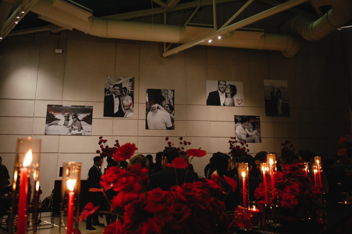 Black-and-white couple photographs hang above candlelit tables filled with red flowers in a dark dining room.