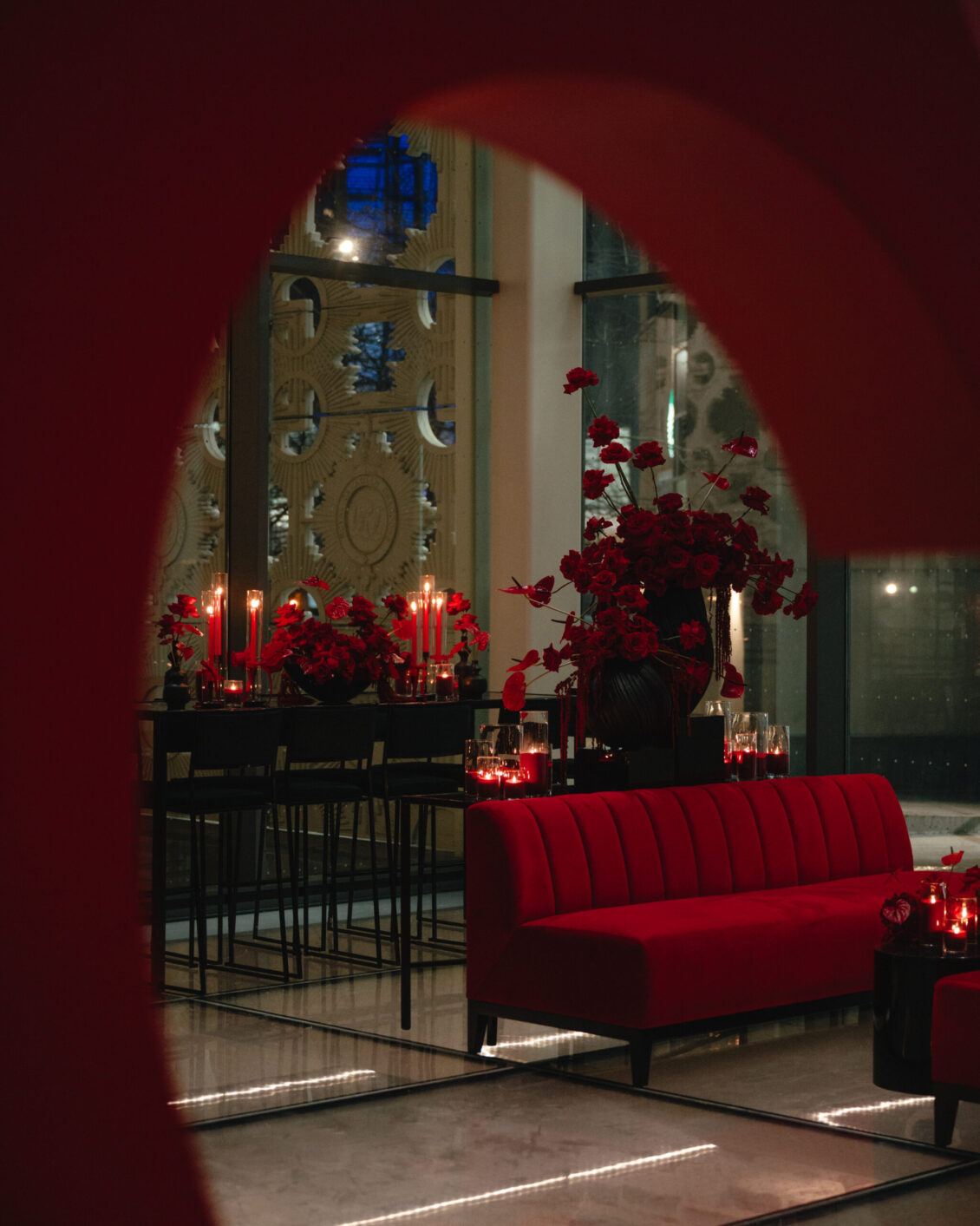 A red heart-shaped opening frames a lounge with red seating, flowers, glossy tables, and candles.