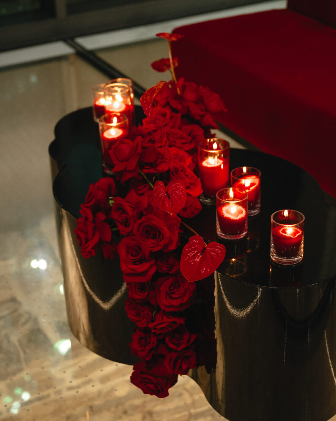 Deep red roses cascade over black stands beside glowing red candles in clear glass holders.