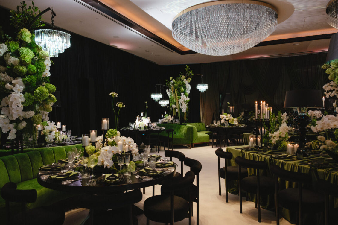 Round tables, black chairs, green banquettes, white flowers, candles, and circular crystal chandeliers fill the reception room.