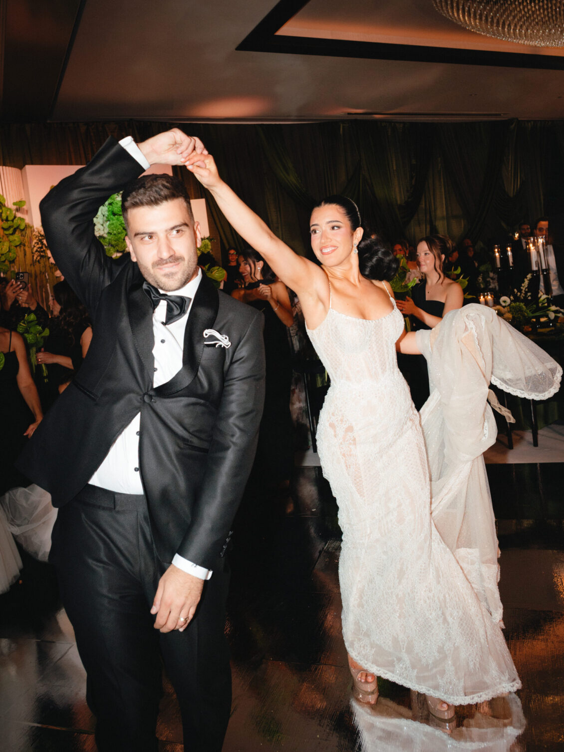 Cosimo leans toward the camera while Valerie smiles behind him with one arm raised and a white cloth overhead.