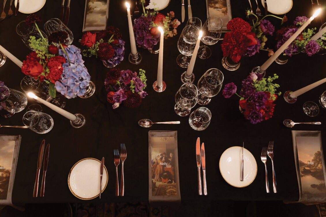 Elegant dinner table set with plates, cutlery, wine glasses, tall candles, and vibrant floral centerpieces in red, purple, and blue hues on a dark tablecloth—perfect for an Irish castle wedding at Ashford Castle.