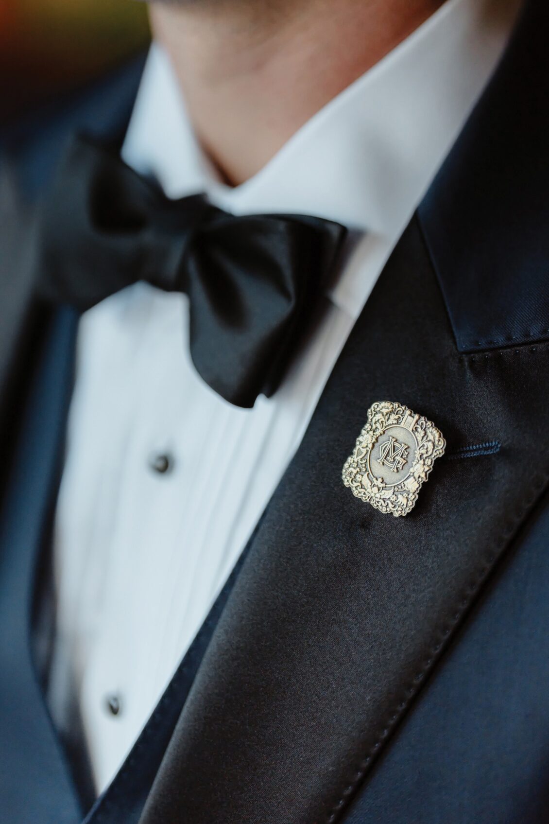 A close-up of a person wearing a black tuxedo jacket, white dress shirt, and black bowtie, with a decorative silver pin attached to the lapel—an elegant ensemble perfect for an Irish castle wedding at Ashford Castle.