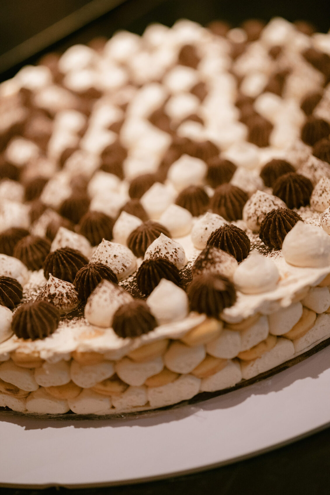 A close-up of a round cake topped with alternating swirls of white and brown cream, dusted with cocoa powder, on a white cake board—perfect for adding a touch of elegance to your Renaissance Phuket wedding.