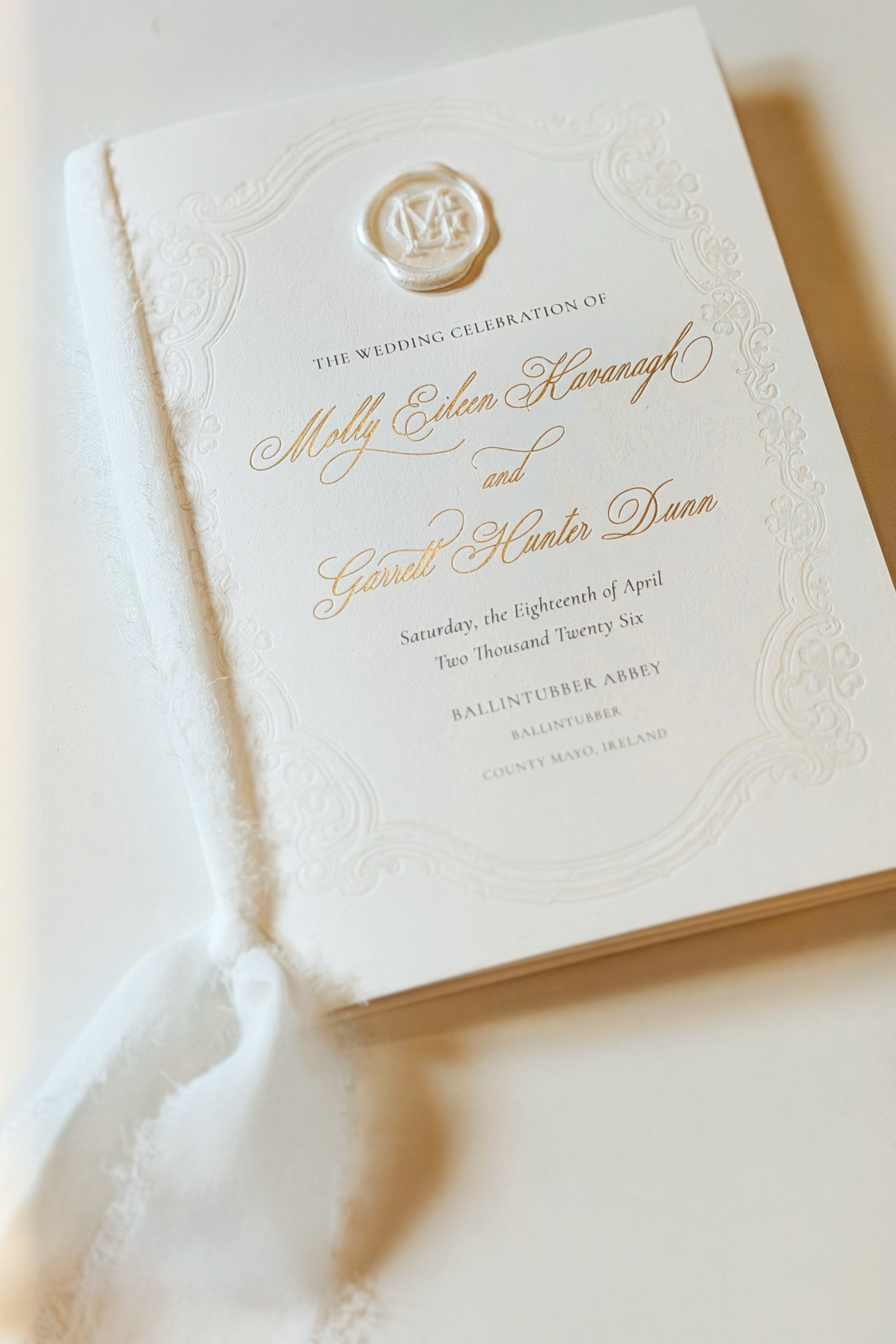 Elegant white wedding program with gold script reading “The Wedding Celebration of Molly Eileen Kavanagh and Garrett Hunter Dunn,” dated April 18, 2026, at Ballintubber Abbey, County Mayo, Ireland.
