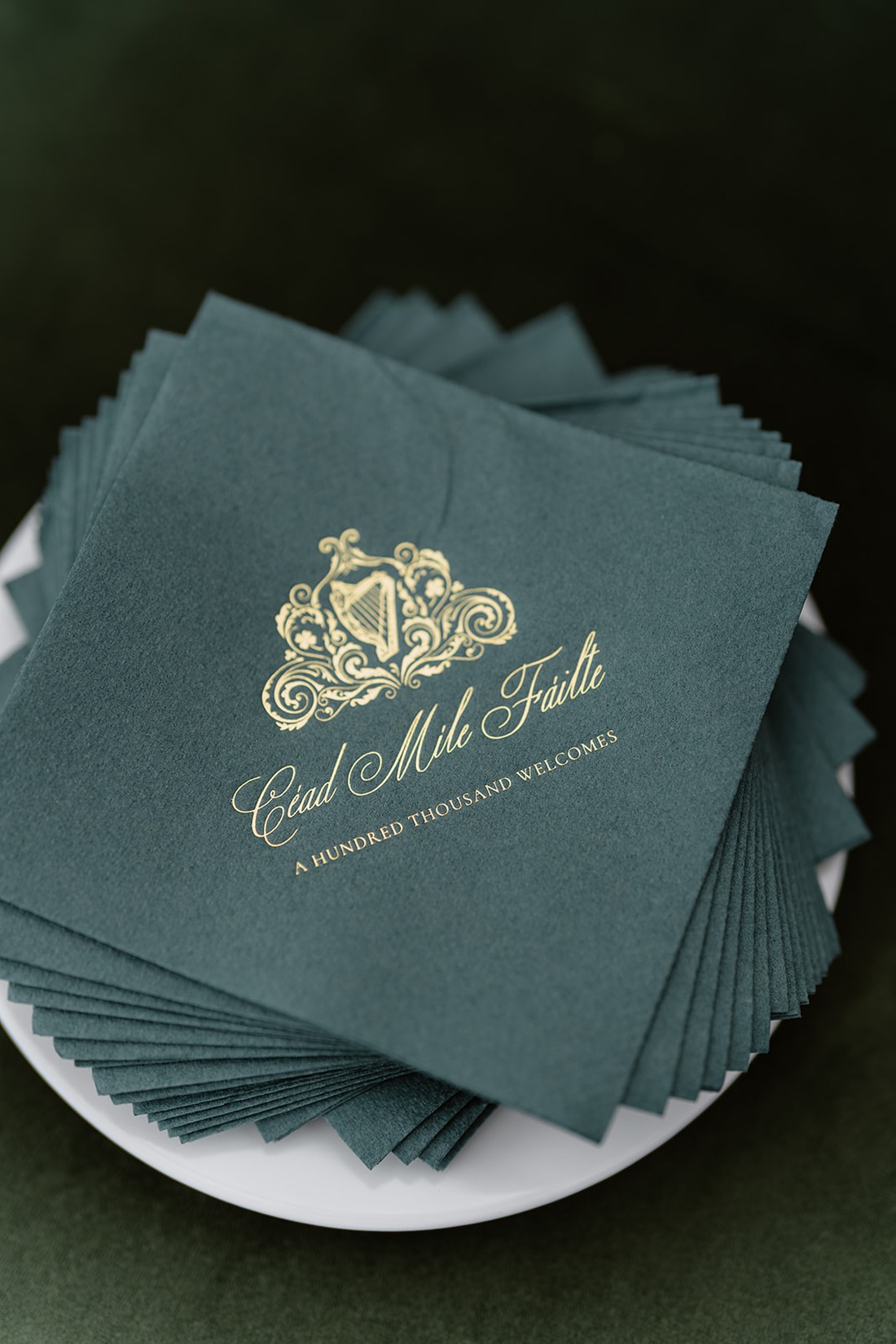 A stack of green napkins with gold script reading “Céad Míle Fáilte” and “A Hundred Thousand Welcomes,” along with a decorative harp design, evokes the elegance of an Irish castle wedding at Ashford Castle, beautifully presented on a white plate.