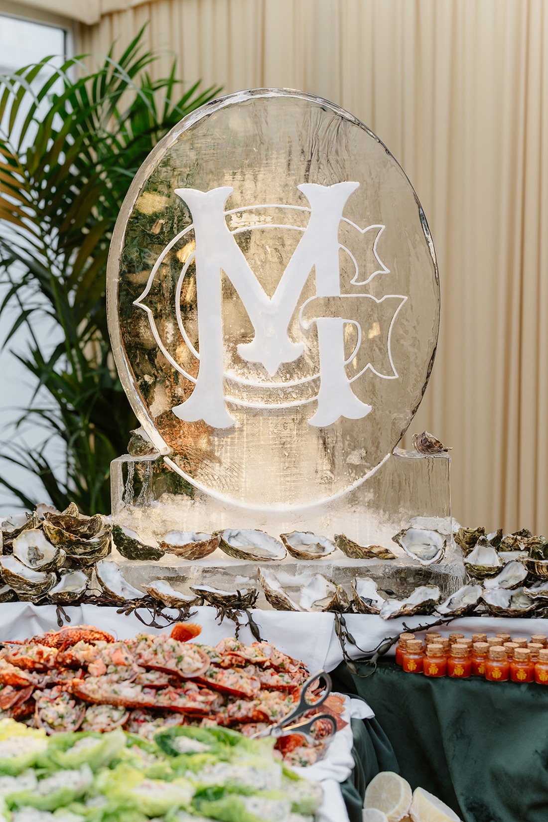 Seafood display with oysters, lobster, and shrimp on a table, featuring a large ice sculpture engraved with the initials “MG” in the background—an exquisite culinary highlight at this Irish castle wedding at Ashford Castle.