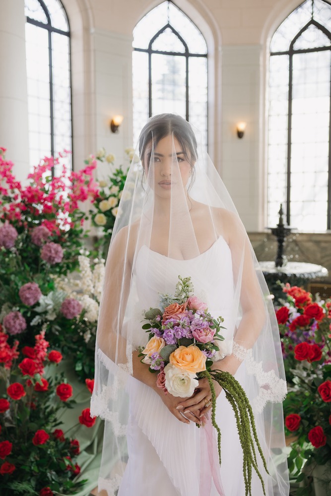 Bride holding a pastel bouquet before Conservatory windows
