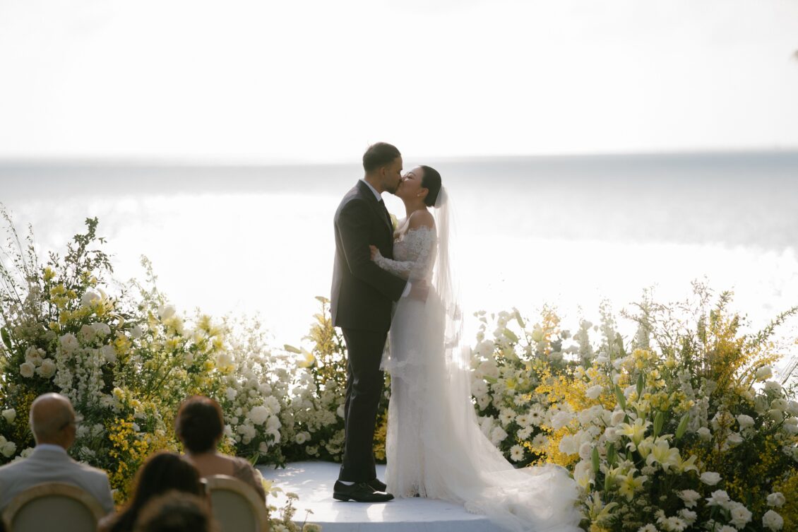 Christine and Shaun's Phuket wedding, wide first-kiss frame resolves the ceremony with florals and waterfront setting intact.
