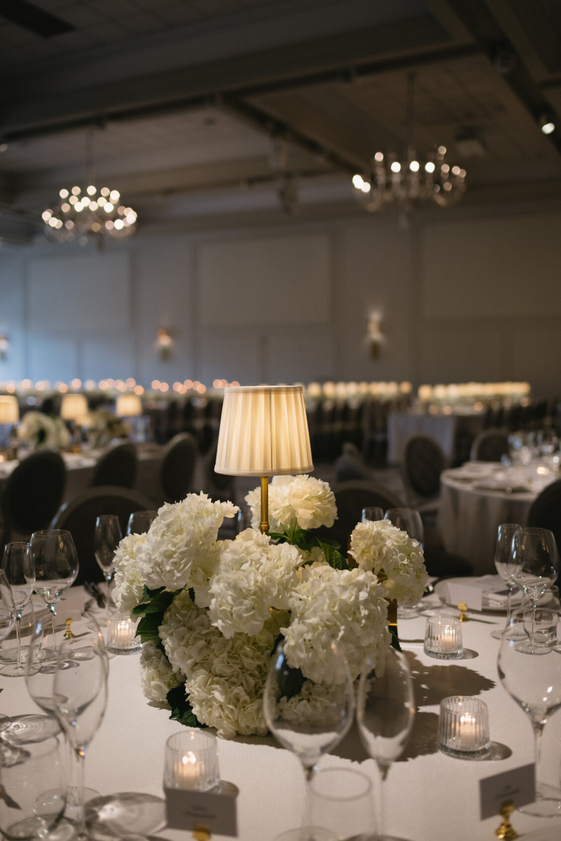 White reception florals arranged around a sculptural table lamp.