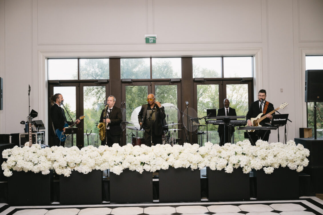 The live band performs behind a bank of white flowers.