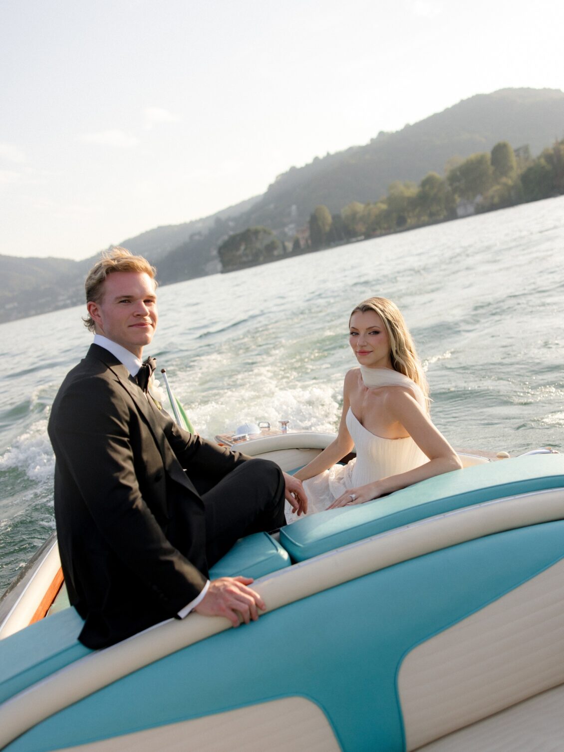 Newlyweds hold hands across a moving boat on Lake Como.