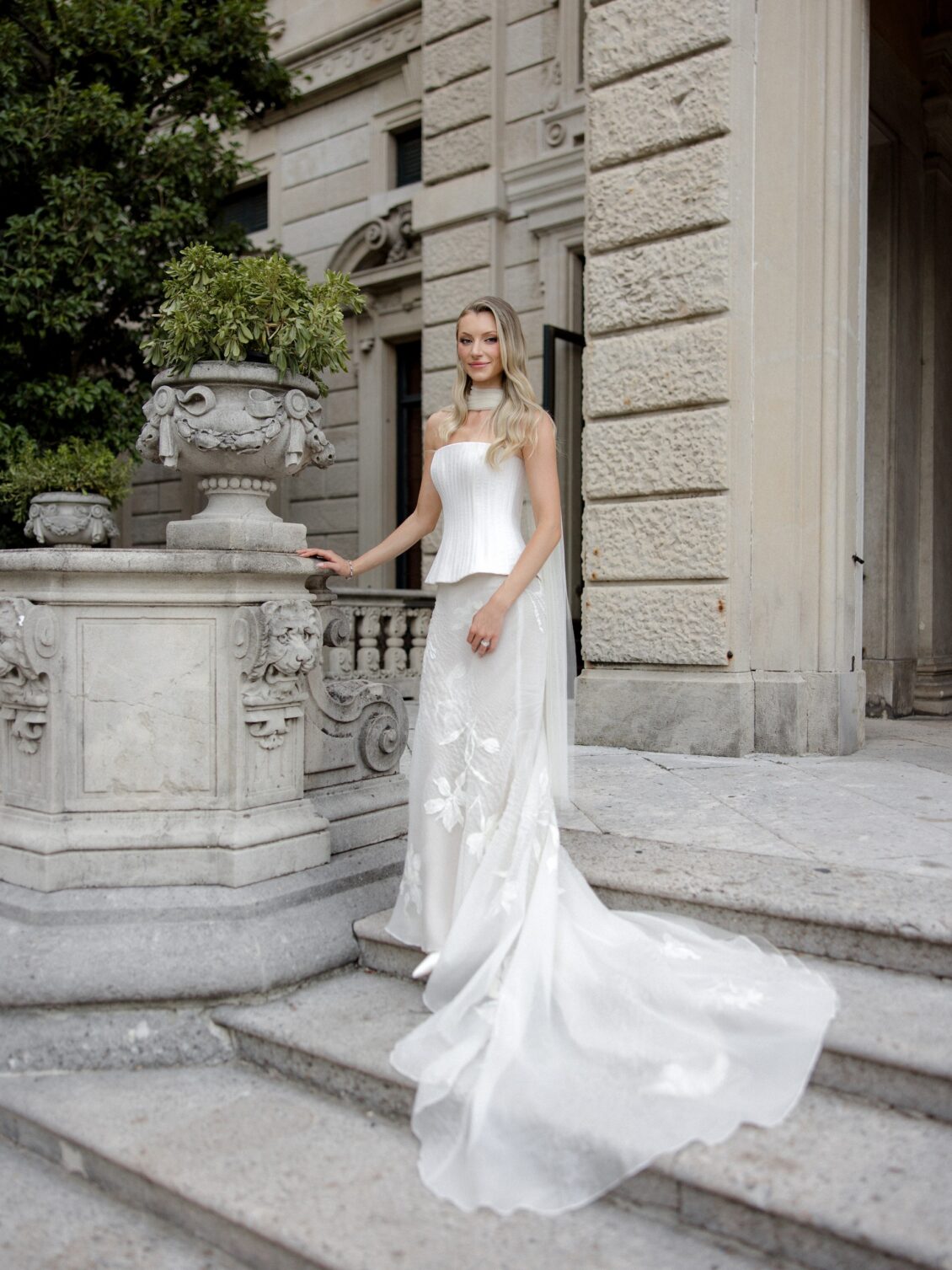 Bride poses on stone steps with her wedding gown train extended.