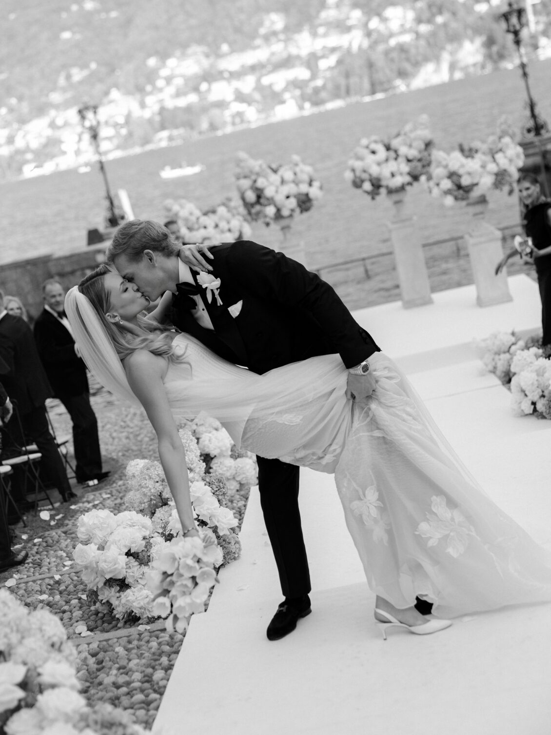 Groom dips and kisses the bride on the flower-lined aisle.