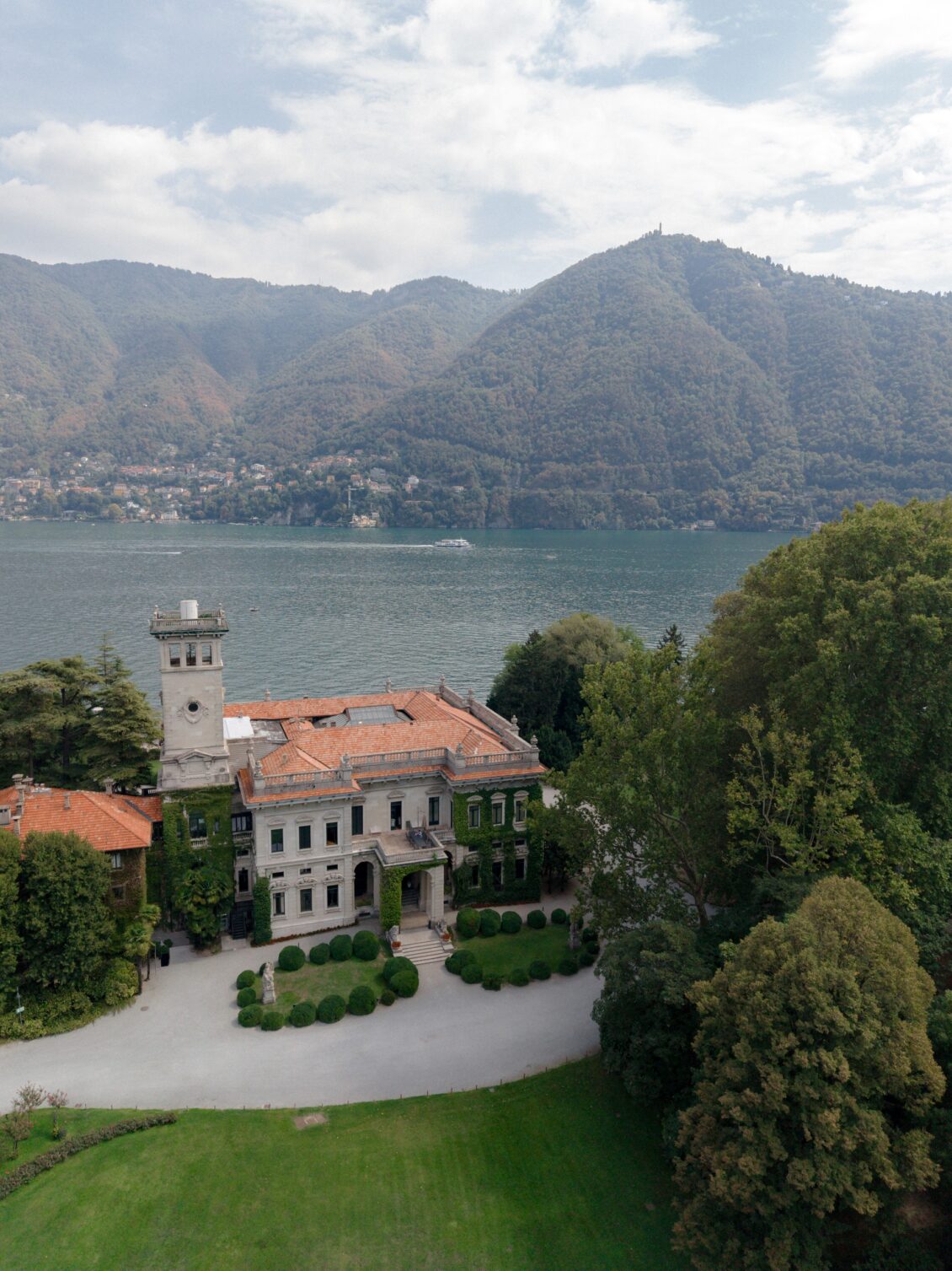 Aerial view of Villa Erba beside Lake Como and forested mountains.