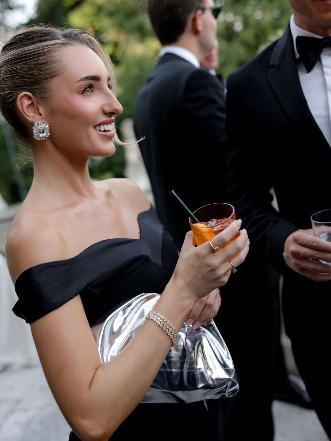 Wedding guest in a black dress holds an orange cocktail.