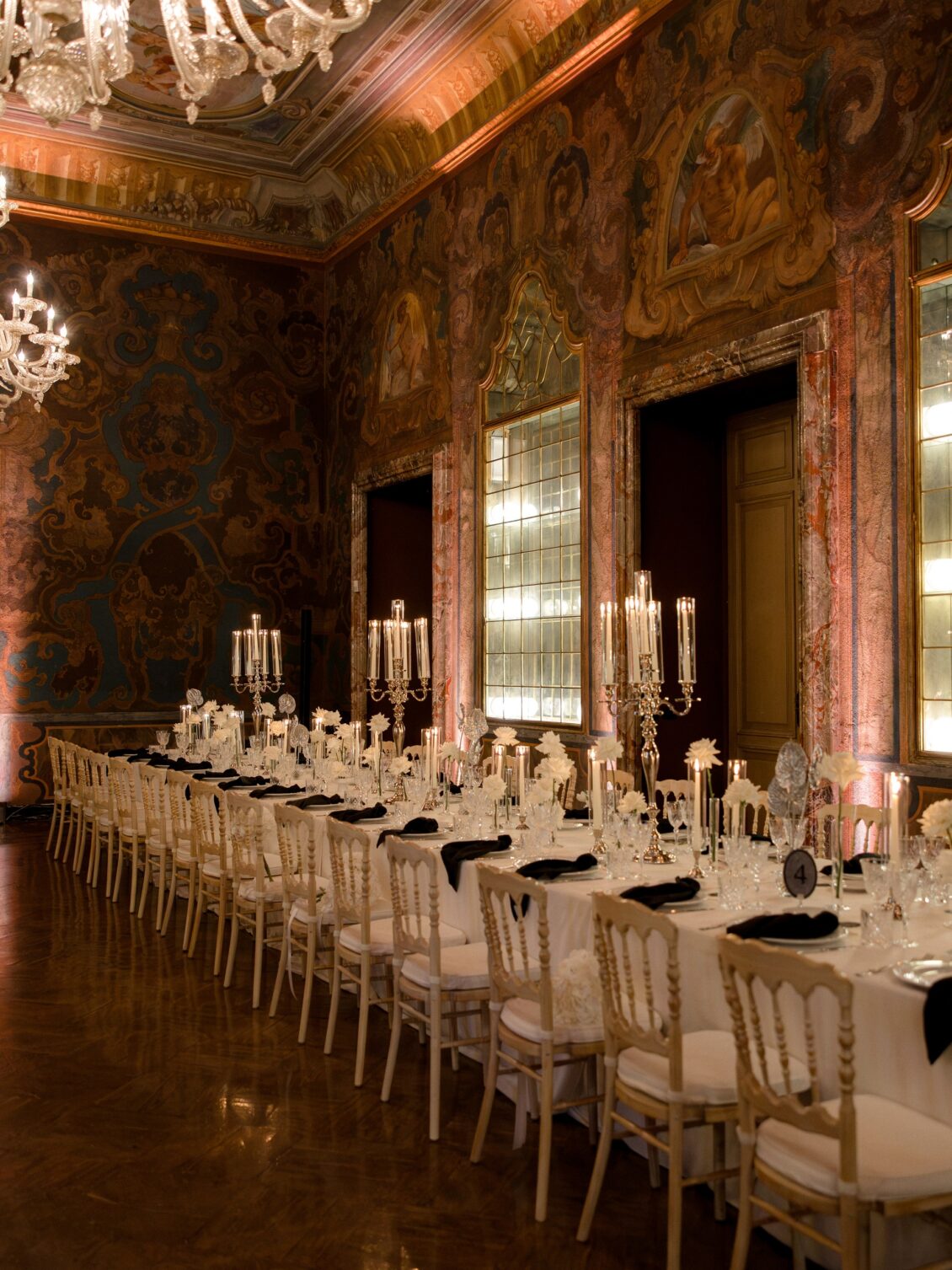 Long reception table beneath chandeliers in an ornate room.