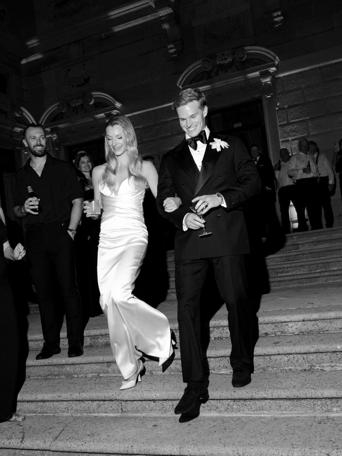 Newlyweds walk down exterior stone steps at night.