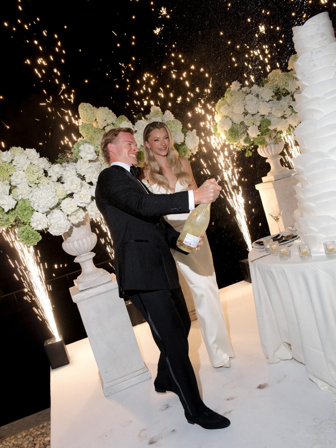 Newlyweds celebrate beside their cake amid fountain sparklers.