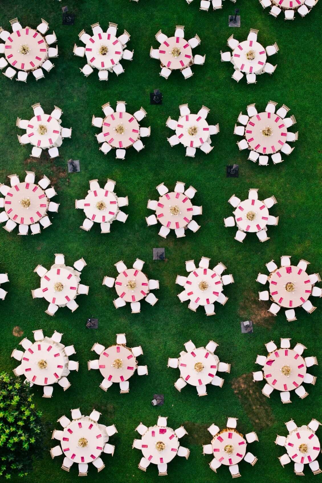 Overhead view of round dinner tables with white chairs and magenta napkins on a green lawn in Rome.