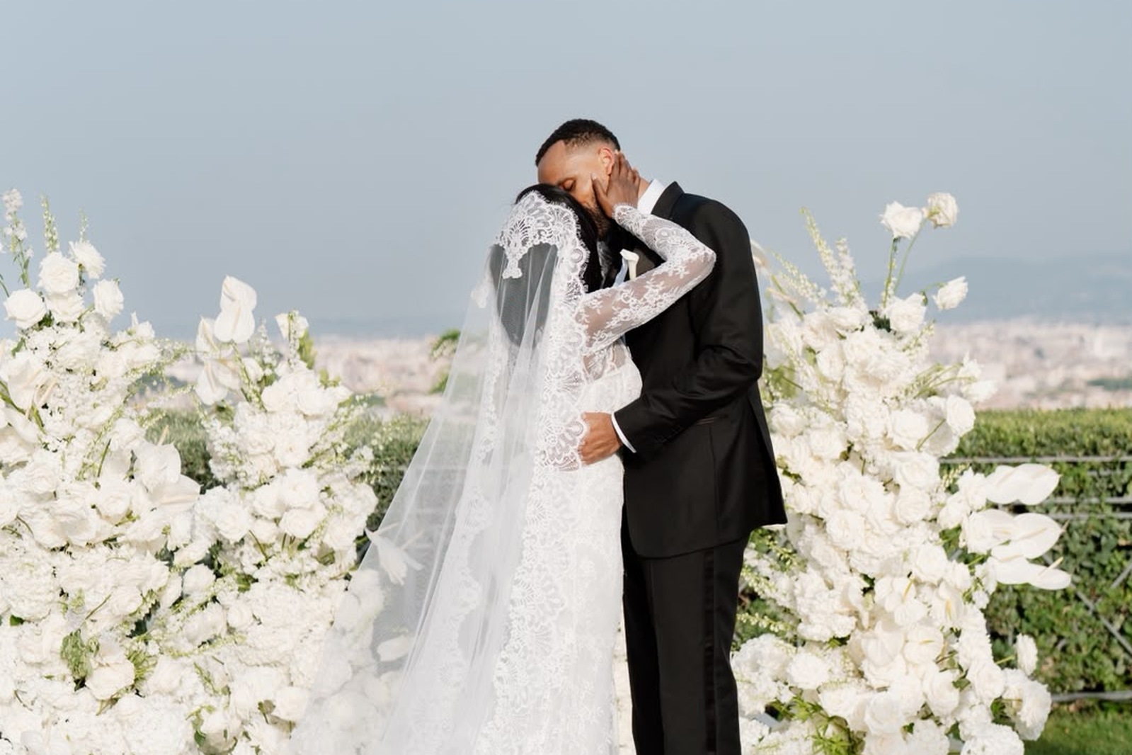 Ugochi and Adefolarin kiss between white flowers during their outdoor wedding ceremony in Rome.
