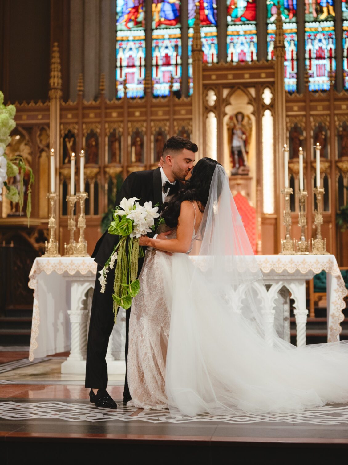 Valerie and Cosimo kiss before the cathedral altar as her long veil, train, and cascading bouquet extend across the patterned floor.