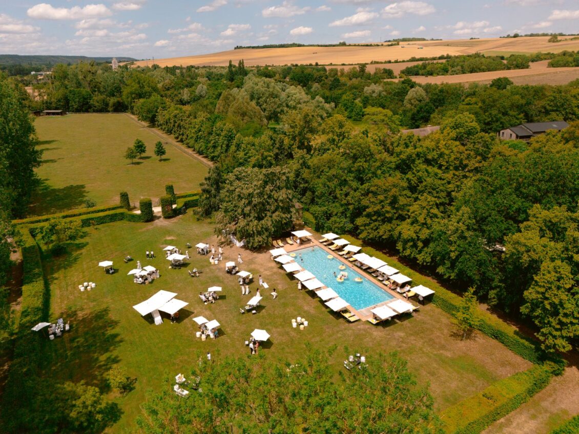 Aerial view of the pool, lawn and parasols set among fields and woodland at Domaine de Primard