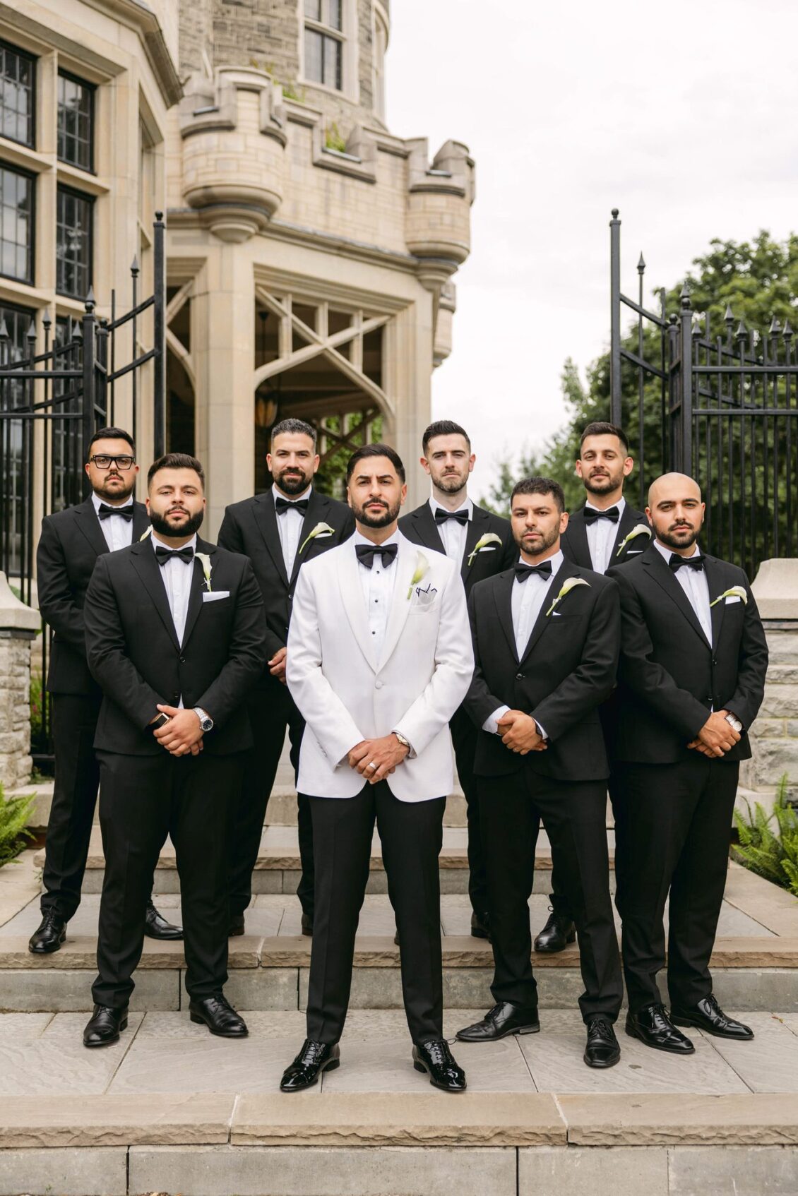 Alex in a white tuxedo jacket with his groomsmen in black tuxedos on stone steps at Casa Loma